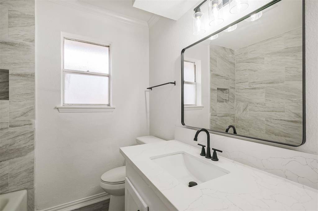 The remodeled hall bathroom features a new vanity with a quartz countertop, a stylish mirror, and an elongated toilet.