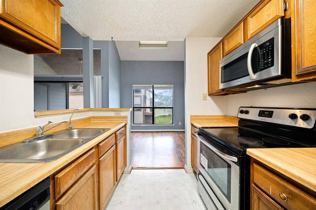 A compact kitchen with wooden cabinets, steel appliances, and a double sink.