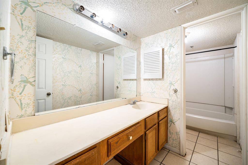 Fearturing a large mirror above a long vanity with ample storage and a tub-shower combo.