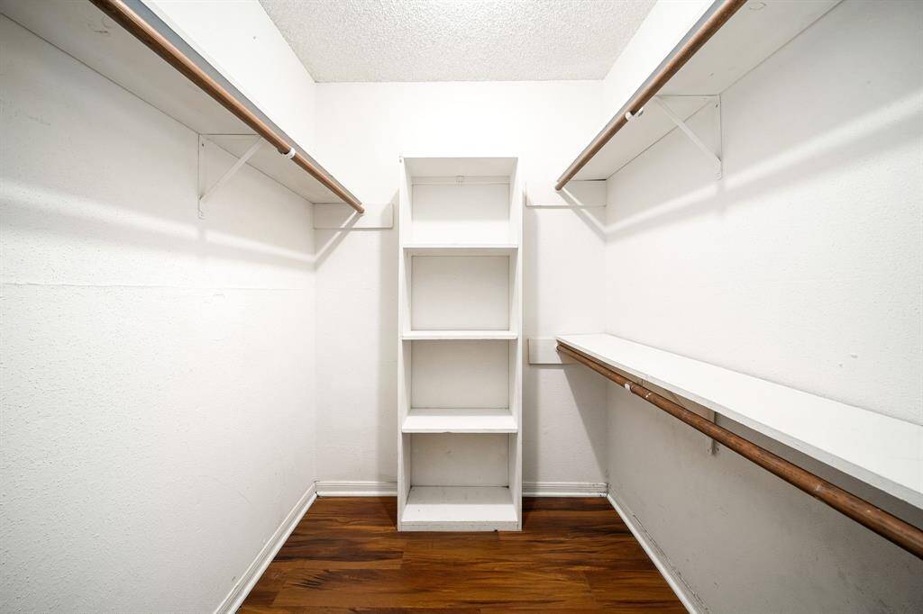 Spacious walk-in closet with wooden flooring, dual hanging rods, and built-in shelving for ample storage.