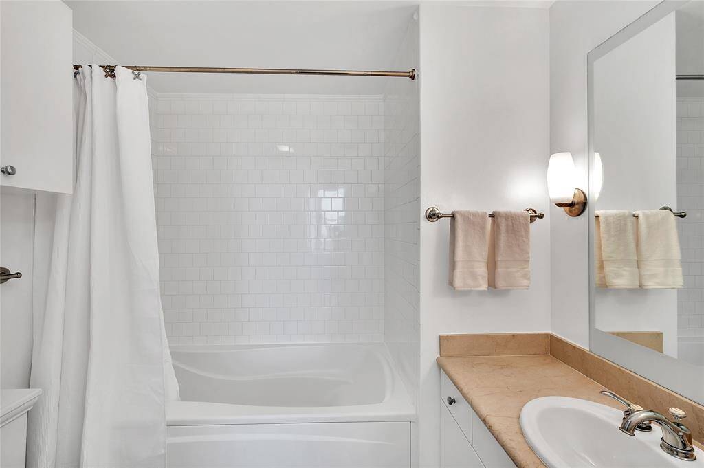 Bathroom has deep soaking tub/shower combination with white tile surround!  Vanity had door and drawer storage with stone countertop.  Note cabinet storage on left above toilet.