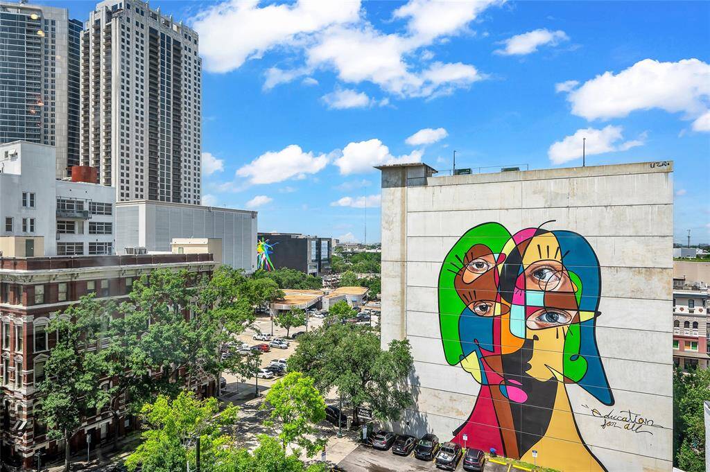 The view from Bayou Lofts 6E showcases historic buildings, modern skyscrapers, treetops, open sky and one of over 40 murals in Downtown Houston entitled "Education For All". This mural by Belin is in Neo-Cubist style and is drawn in one continuous line! What a colorful addition to the view!