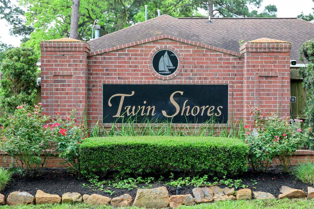 The photo features a welcoming entrance sign for "Twin Shores," set against a backdrop of neatly trimmed greenery and colorful flowers, in a well-maintained community.