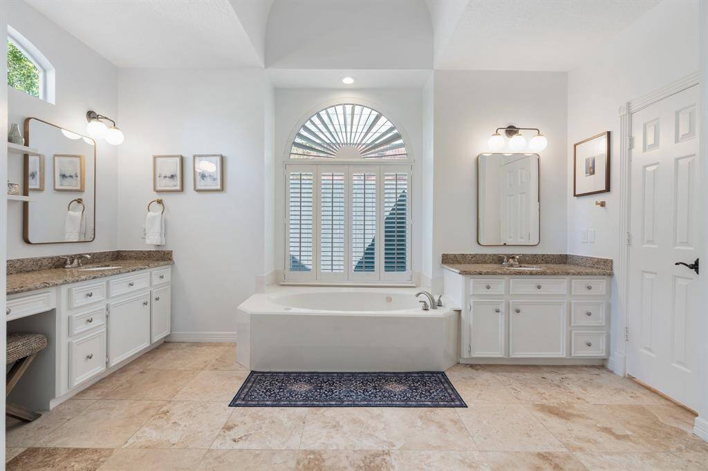 Updated mirrors, lighting and hardware add a touch of flair to a spacious primary bath with spa tub, stand alone shower and closet complete with built-in storage.