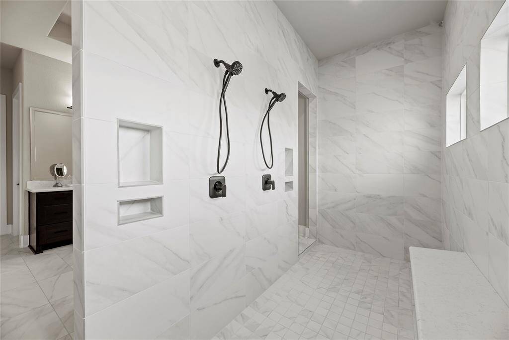 Matching tile work in the shower provides consistency in design. Early mornings are made brighter and warmer in the spacious shower featuring recessed lighting and a built-in shelf for self-care items!