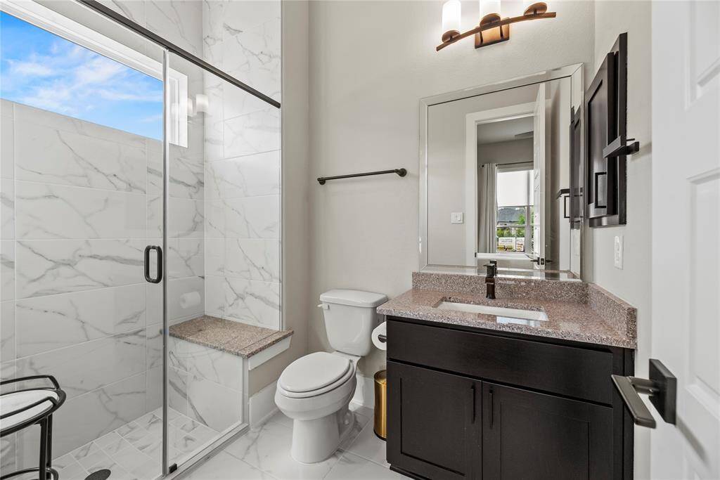 This elegant bathroom features a sleek, glass-enclosed shower that maximizes natural light and adds a modern touch. The space is completed with a polished vanity, stylish mirror, and contemporary lighting, creating a serene and sophisticated atmosphere.