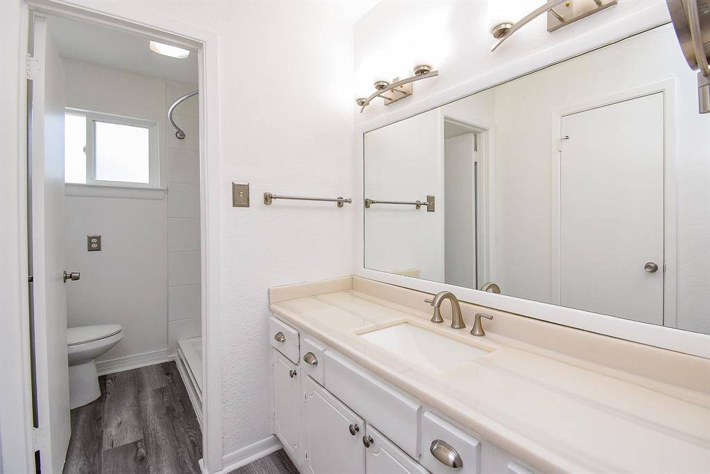 The Primary Bathroom highlights laminate floors, white cabinets, tile countertops, and a large mirror with gorgeous vanity lights.