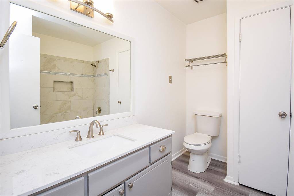 Lovely Secondary Bathroom featuring laminate floors, granite countertop and light cabinets, a large mirror, and vanity lights.