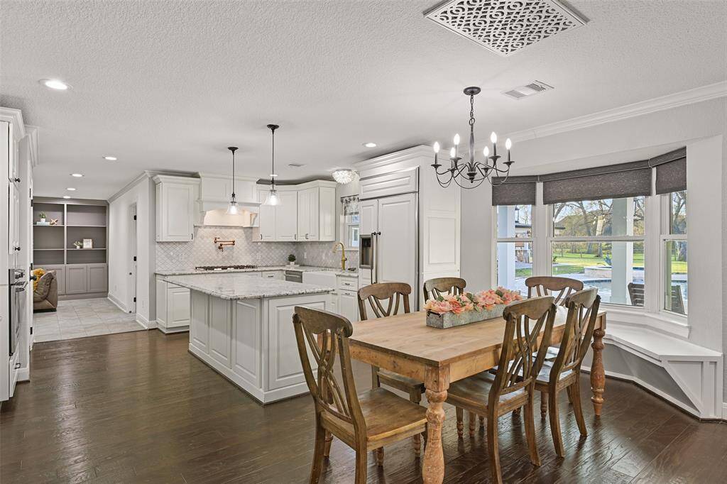 Just beyond the living room space and open to the kitchen, you'll find this casual dining space that showcases a stylishly updated candelabra chandelier, wood floors neutral paint trimmed with crown molding, and a bay window seat overlooking the pool and acreage beyond.