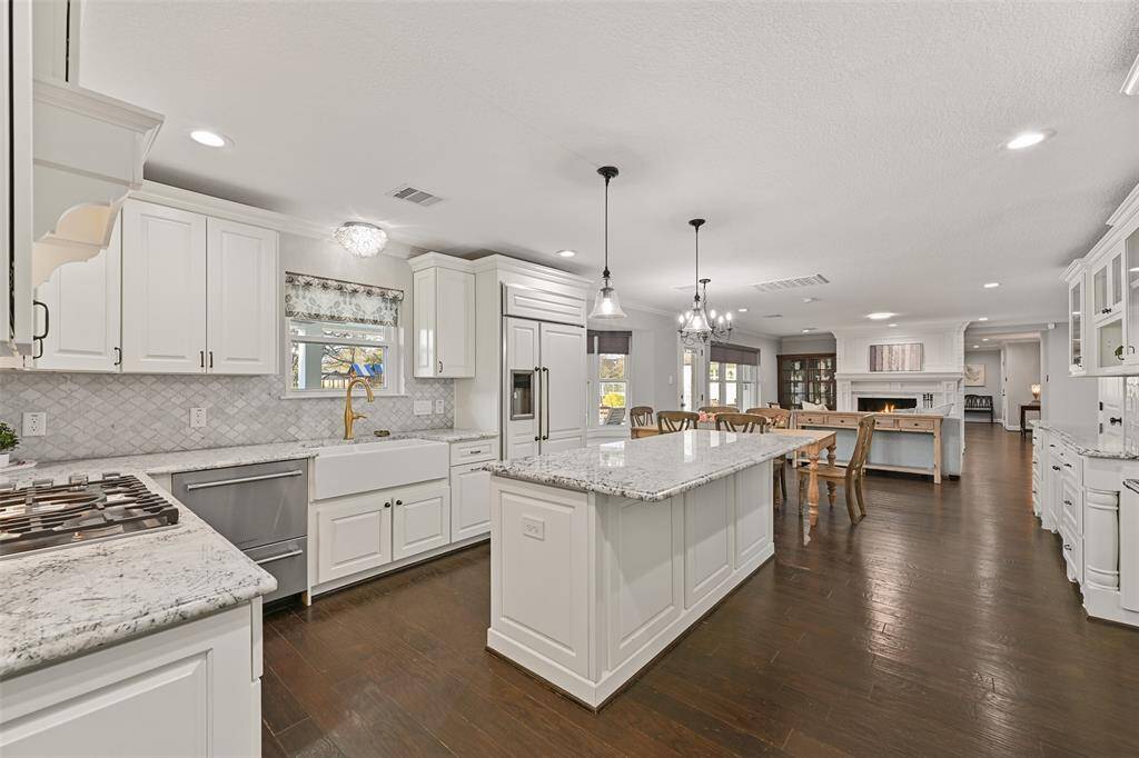 The island kitchen has been magnificently recreated with impressive finishes that include gorgeous granite countertops, an arabesque-shaped marble tile backsplash, designer lighting, and custom white soft-close cabinetry with coordinating cabinet faces on the refrigerator.