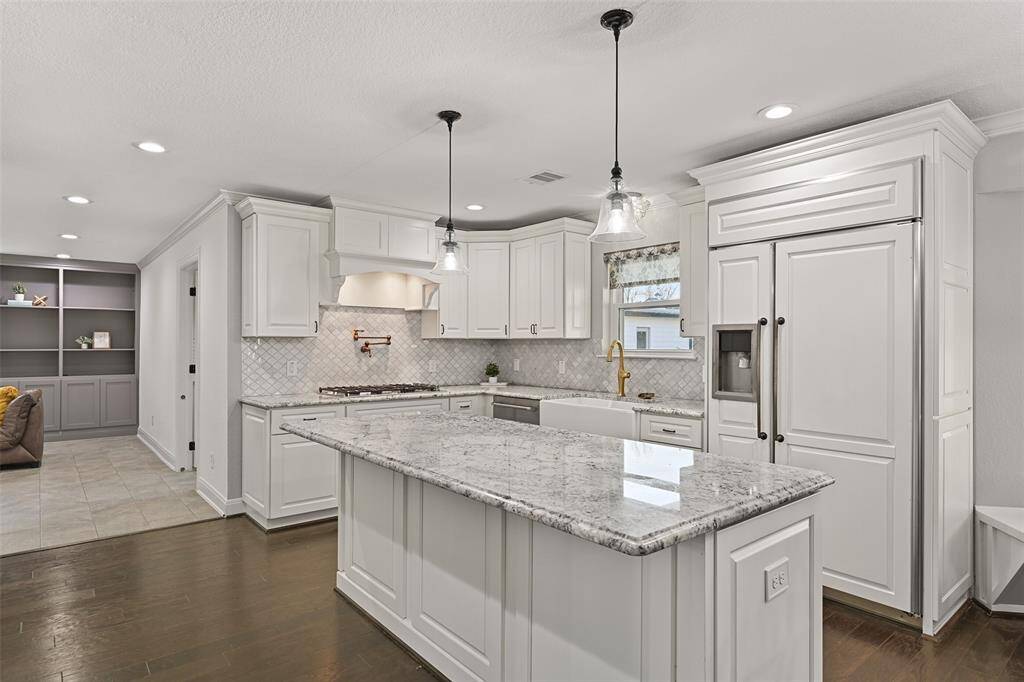 The island kitchen has been magnificently recreated with impressive finishes that include gorgeous granite countertops, an arabesque-shaped marble tile backsplash, designer lighting, and custom white soft-close cabinetry with coordinating cabinet faces on the refrigerator.