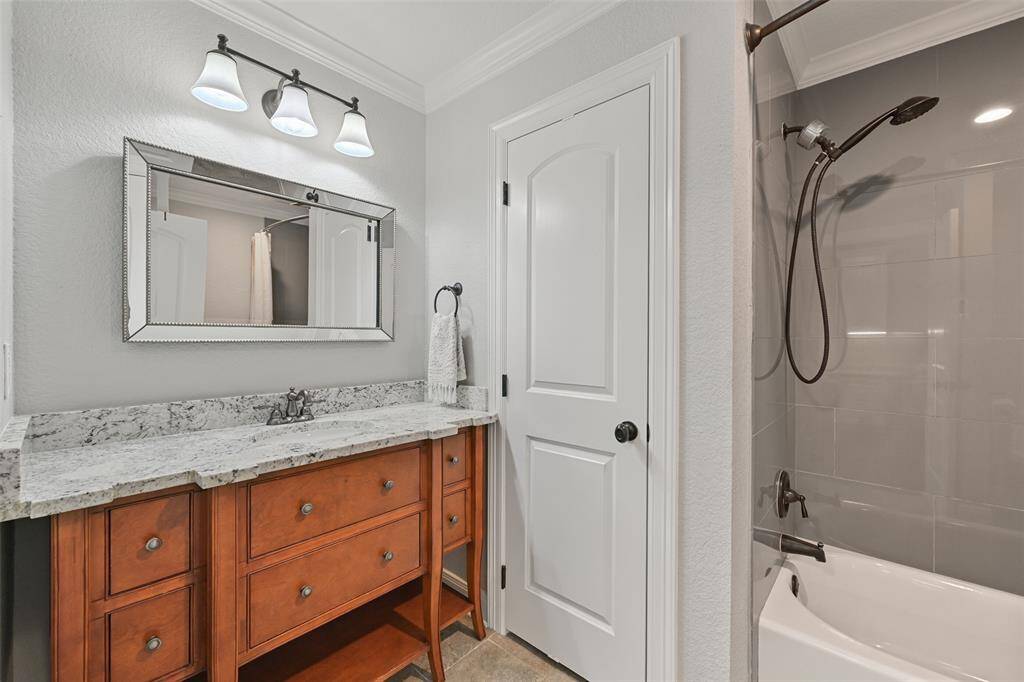Another full bathroom is available off of the owners' home office area and this one boasts a dresser-style vanity with a granite countertop, a single undermount sink, a beveled frame mirror, designer lighting, tile floors, and a combination bathtub and shower with a handheld showerhead and a tile surround.