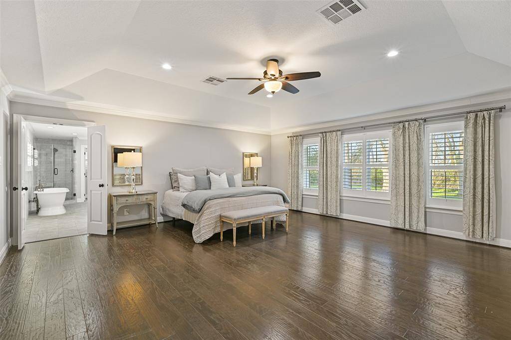 Escape to the serenity of this secluded owners' suite and notice the elevated gambrel ceiling with recessed lights and a lighted ceiling fan, handsome engineered wood floors, neutral grey paint trimmed with crisp white crown molding, and a wall of rear-facing windows dressed with timeless plantation shutters.