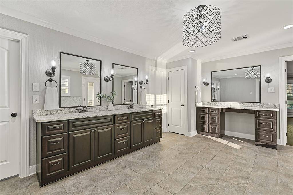 Elegance abounds in this must-see master bathroom with a lengthy granite top vanity with dual undermount sinks, ample espresso-stained cabinetry, framed mirrors, sconce lights, and a separate seated vanity space.