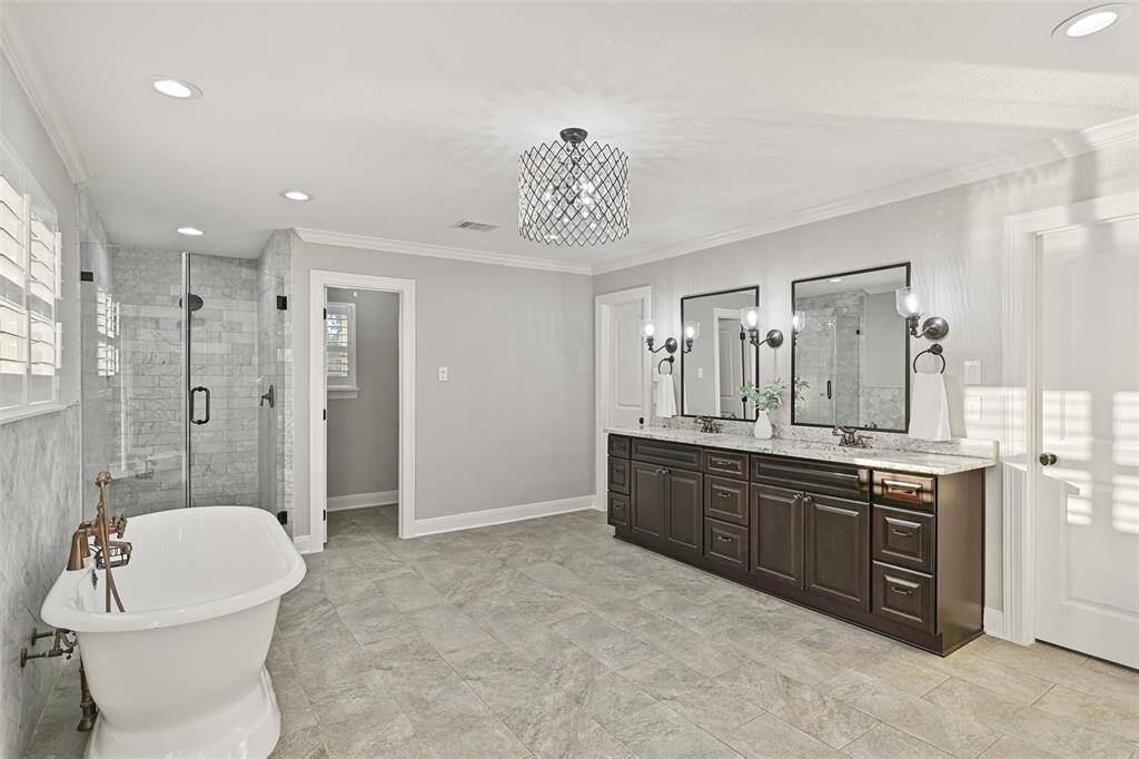 Relaxation awaits beneath the deep waters of this freestanding soaker tub with a wall-mounted bronze faucet & handheld sprayer and a marble tile splash wall that extends into the seamless glass shower with a bench seat.