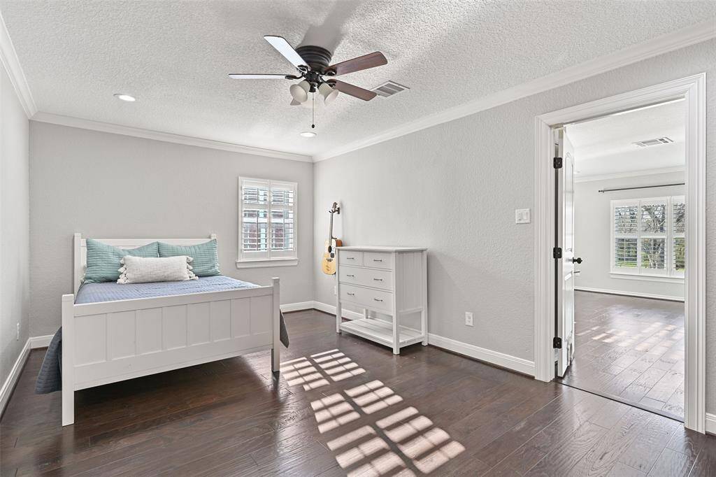 The first of four secondary bedrooms on the second floor is accessible via the hallway or the gameroom and it boasts a lighted ceiling fan, recessed lights, neutral grey paint trimmed with crisp white crown molding, and a window with plantation shutters.