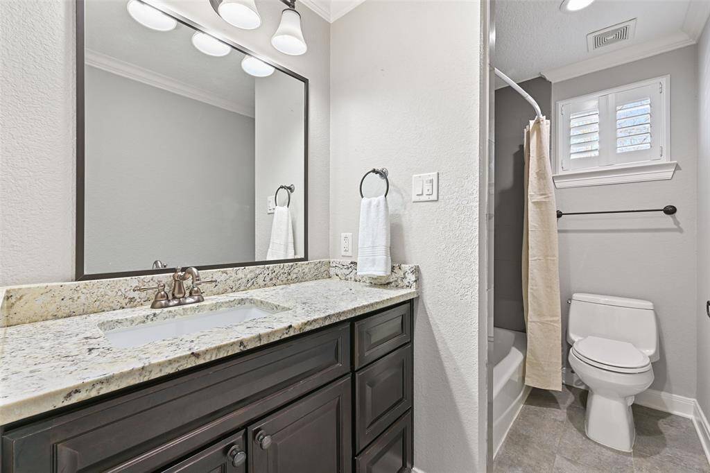 This bathroom services two of the upstairs bedrooms and it showcases a black painted vanity topped by a granite countertop, a rectangular basin sink, a framed mirror, updated lighting, tile floors, and a combination bathtub and shower with a tile surround.
