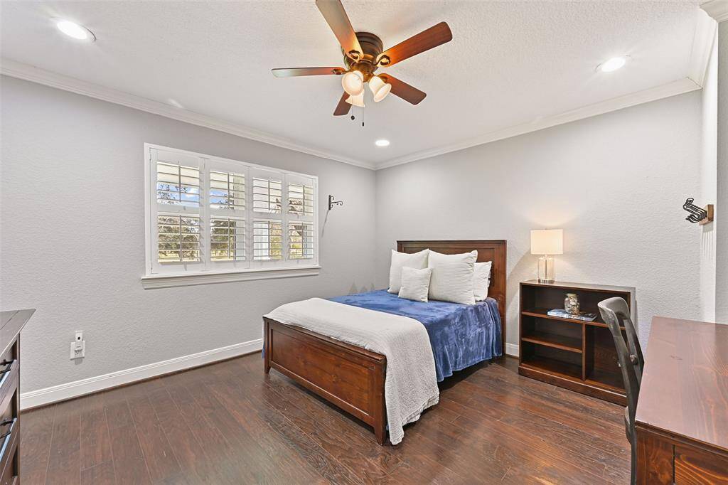 The fifth and final bedroom in the main home has all of the same amenities as the others, including wood floors, neutral paint, crown molding, a lighted ceiling fan, recessed lights, and a window with plantation shutters and front porch views.