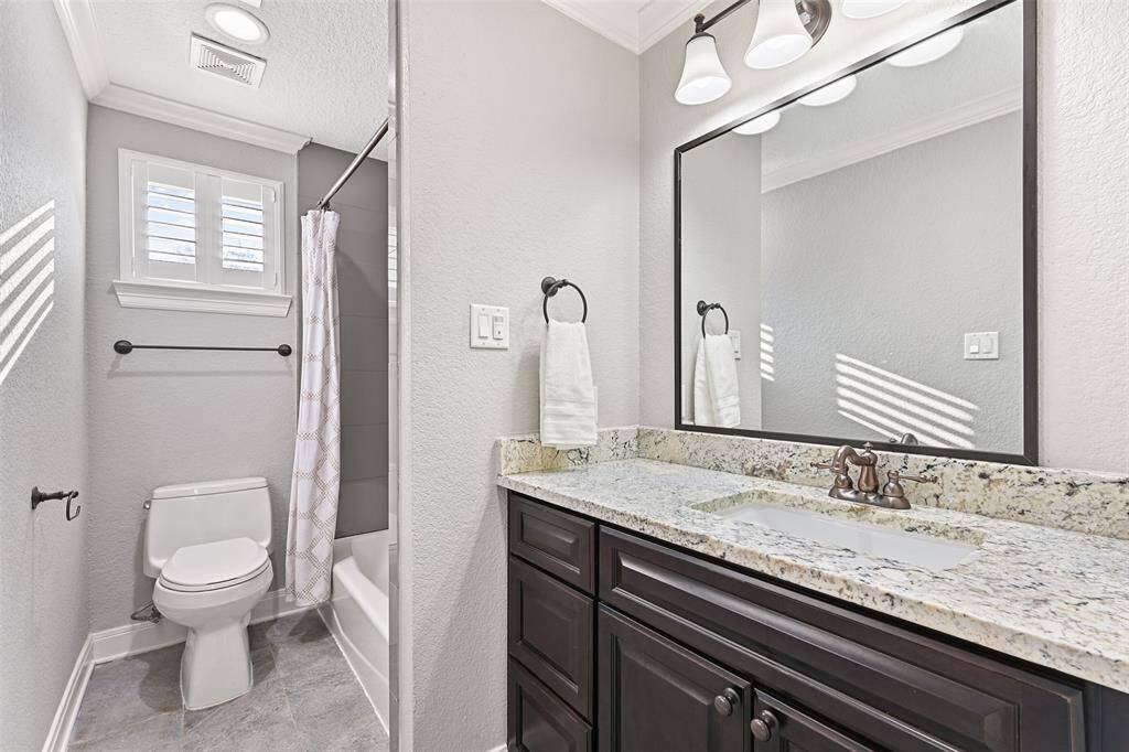 This bathroom services the remaining two secondary bedrooms and it also offers a granite top vanity with a rectangular basin sink, black painted cabinetry, a framed mirror, tile floors, and a combination bathtub and shower with a tile surround.