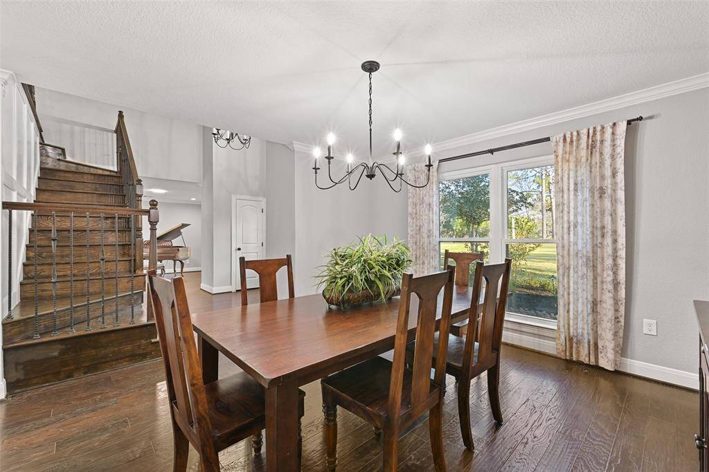 To the left, the foyer spills into this bright and inviting formal dining room that boasts a simple and modern candelabra chandelier, engineered wood floors, neutral paint, crisp white crown molding, and an expansive front-facing window.