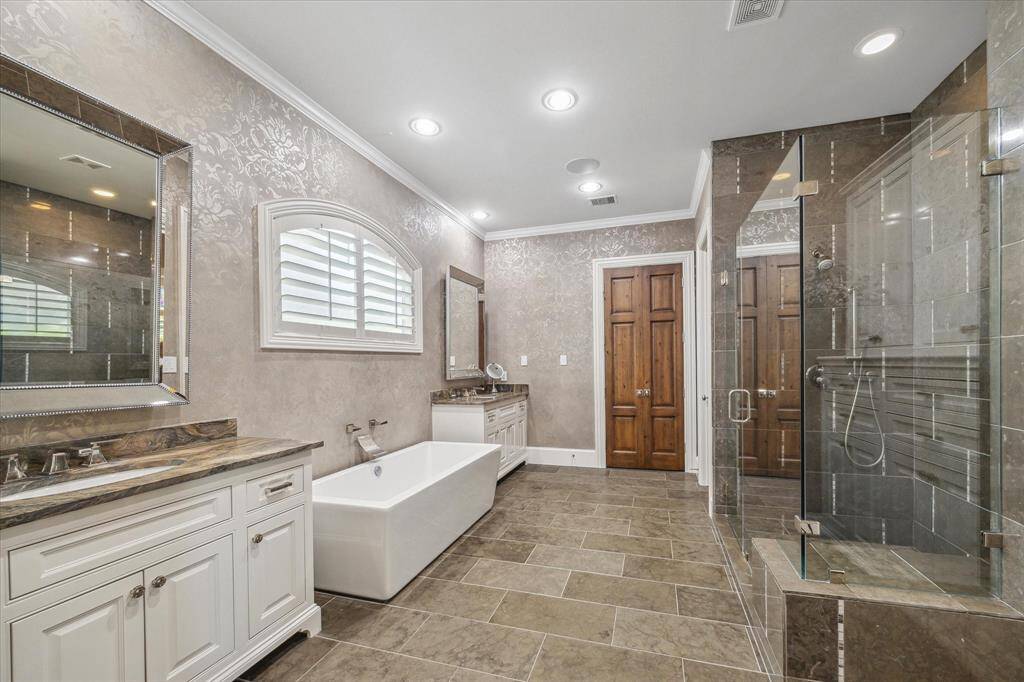 Primary bath featuring a sleek soaking tub, double vanities, and large walk-in shower with frameless shower door.