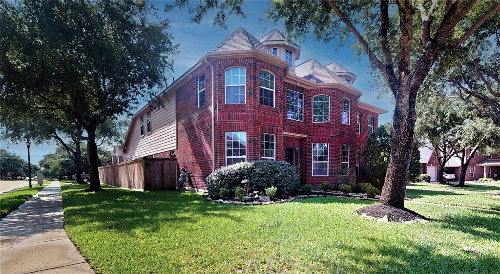 Charming corner lot home with inviting curb appeal, surrounded by lush greenery and mature trees.