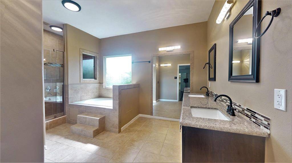 Experience luxury in the newly updated primary bathroom, featuring double sinks, a jacuzzi tub with steps, a dual shower head, and an expansive wall mirror.