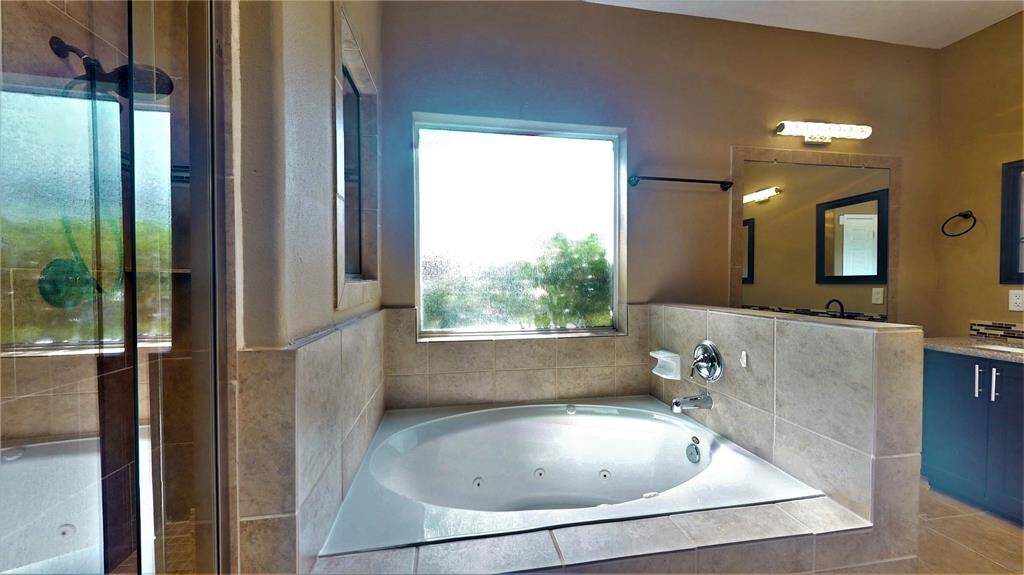 Experience luxury in the 2021-updated primary bathroom featuring double sinks, a jacuzzi tub with steps, a dual shower head, and a large wall mirror.
