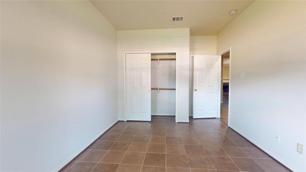 This room features neutral walls and tiled flooring, with a double-door closet and an adjacent door leading to another space. It's bright and versatile, ideal for a bedroom or office.