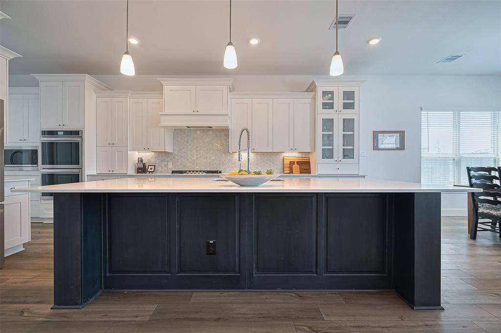 The kitchen features a spacious island with Quartz counters, pendant lighting, white cabinetry, stainless steel appliances, and a bright, open layout with ample natural light.