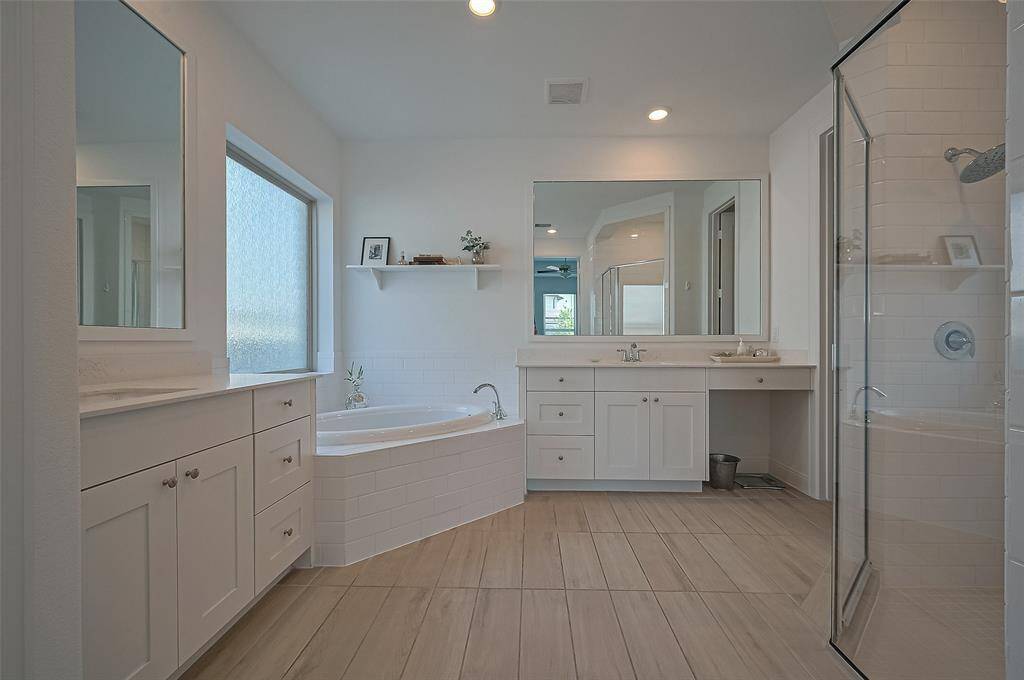 This spacious, modern bathroom features a large soaking tub, a glass-enclosed shower, dual sinks with ample counter space, and elegant cabinetry. Natural light fills the room through a frosted window, creating a bright and inviting atmosphere.