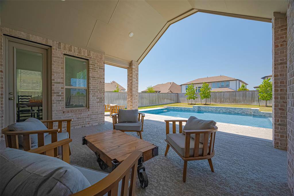 This photo showcases the covered patio with comfortable seating area, overlooking the serene backyard pool.