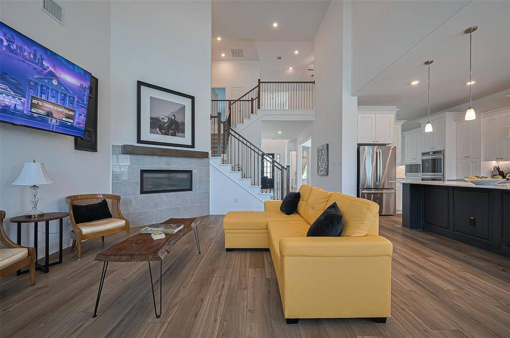 This photo showcases a modern, open-concept living area with high ceilings, continuation of the engineered hardwood flooring, a sleek, corner fireplace, and wall-mounted TV. The space seamlessly connects to the Oversized Island Kitchen.