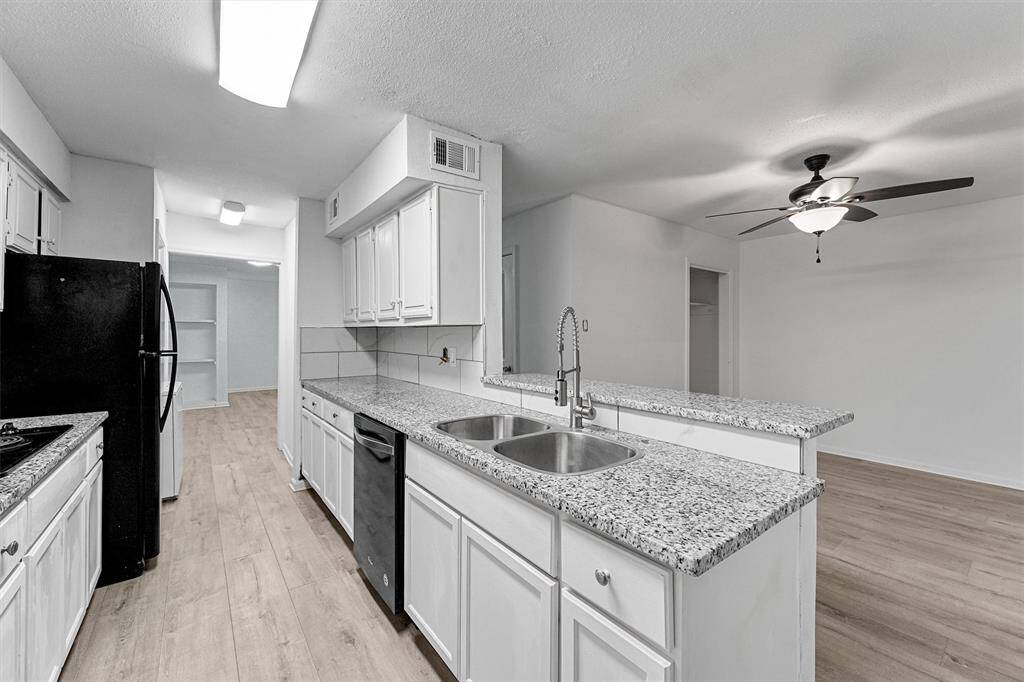 This photo showcases a modern kitchen with granite countertops, white cabinetry, and stainless steel appliances. The open layout includes a ceiling fan in the adjacent living area, and light wood flooring adds warmth to the space.