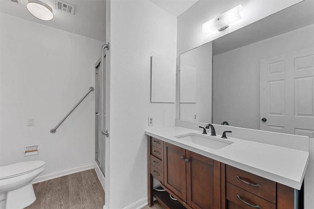 This modern bathroom features a sleek vanity with a large mirror and elegant fixtures. It includes a spacious shower, a toilet, and a grab bar for safety. The design is clean and functional.