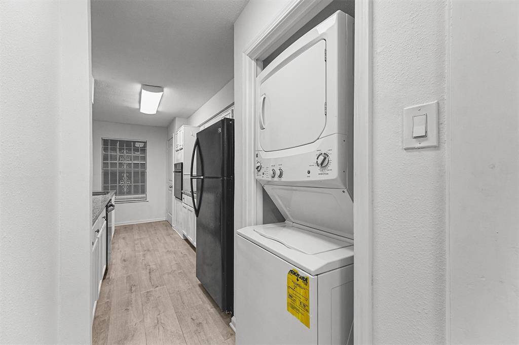 A modern kitchen with white cabinetry and refrigerator. A stackable washer and dryer are conveniently tucked into a closet.