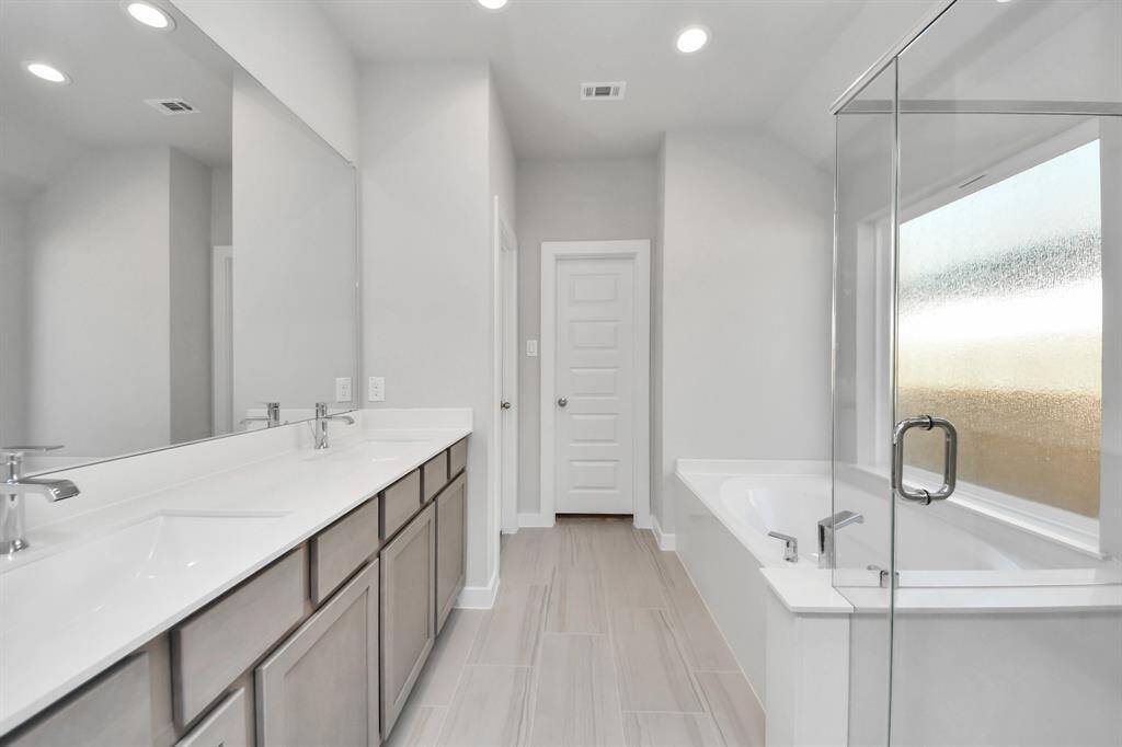 Escape to a spa-like oasis in this primary bathroom. Enjoy a walk-in shower with tile surround, a separate garden tub with custom detailing, and an elegant vanity featuring light countertops, modern hardware, and beautiful recessed lights. Experience luxury and relaxation in every detail. Sample photo of completed home with similar floor plan. Actual colors and selections may vary.