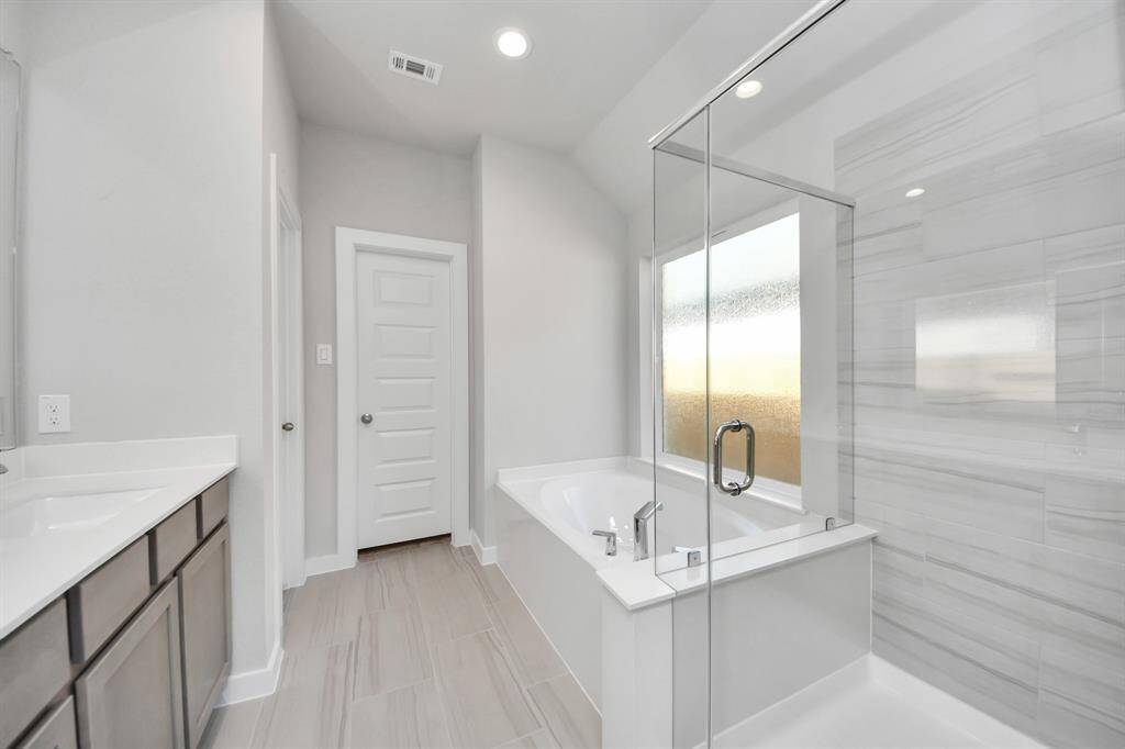 Delight in a spacious walk-in shower enveloped in stylish tile surround, unwind in a separate garden tub adorned with custom detailing. Sample photo of completed home with similar floor plan. Actual colors and selections may vary.