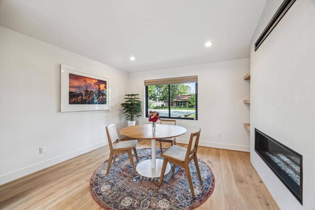 The dining room features a large picture window dressed with Hunter Douglas top-down, bottom-up woven wood burlap Roman shades, and a double-sided gas fireplace that adds to the ambiance.