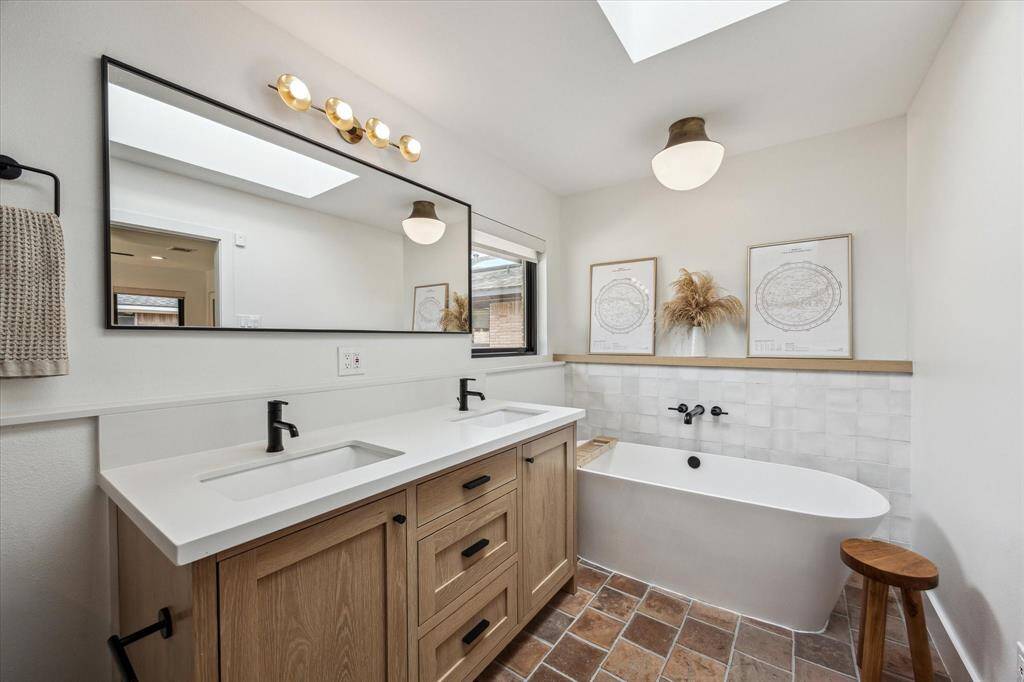 The ensuite bath boasts an oversized soaking tub, custom white oak vanity & shelving, Zellige tile in the shower and along the wall behind the tub, Arto concrete tile floor, brass lighting and custom skylight.