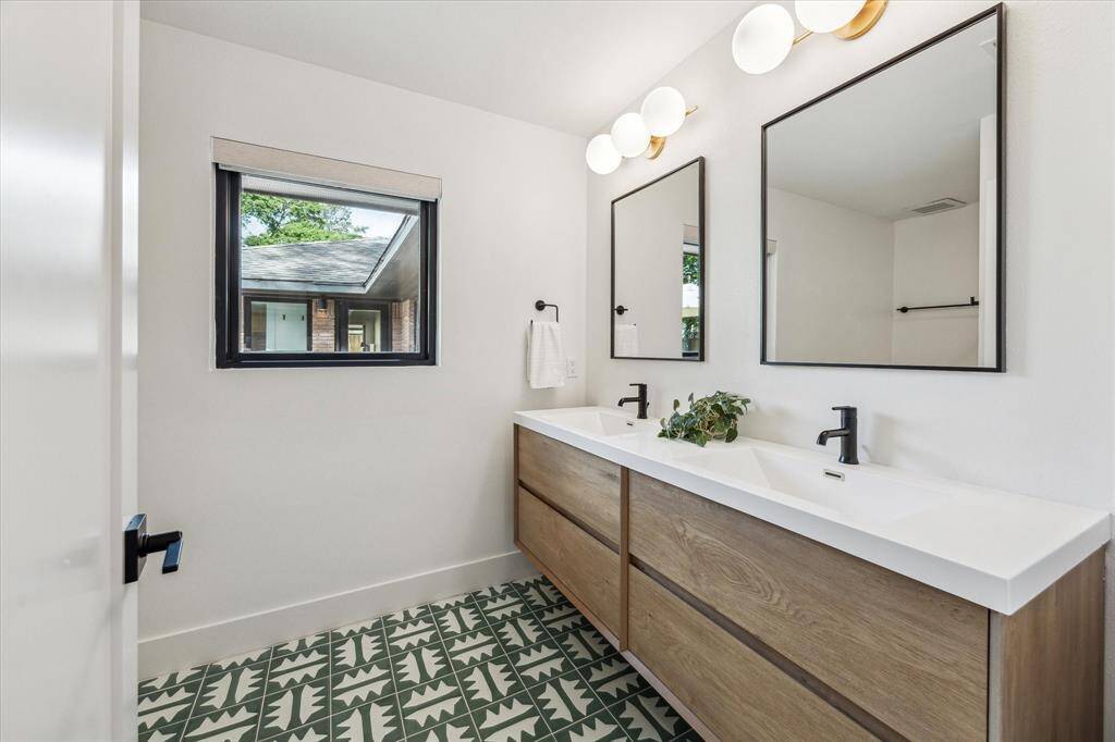 Hall bath featuring distinctive green clay tile hand-painted in Oaxaca, Mexico on the floors and zellige tile backsplash with matt black hardware and brass lighting from West Elm.