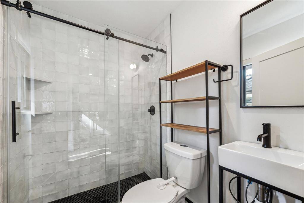 Full bath located outside of the third bedroom and near the back door (can be used as a pool bath) with a glass enclosed shower and black hardware and fixtures.