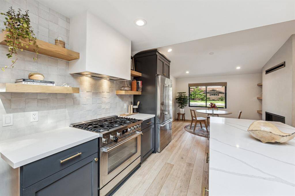 Custom oak shelving flanks both sides of the limewash vent hood over a 6-burner gas stove.