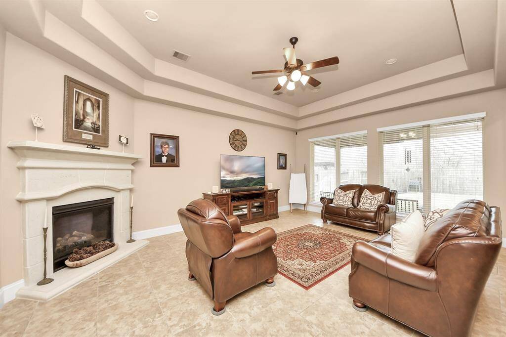 Large living room with a wall of windows, trayed ceilings, and gaslog fireplace.