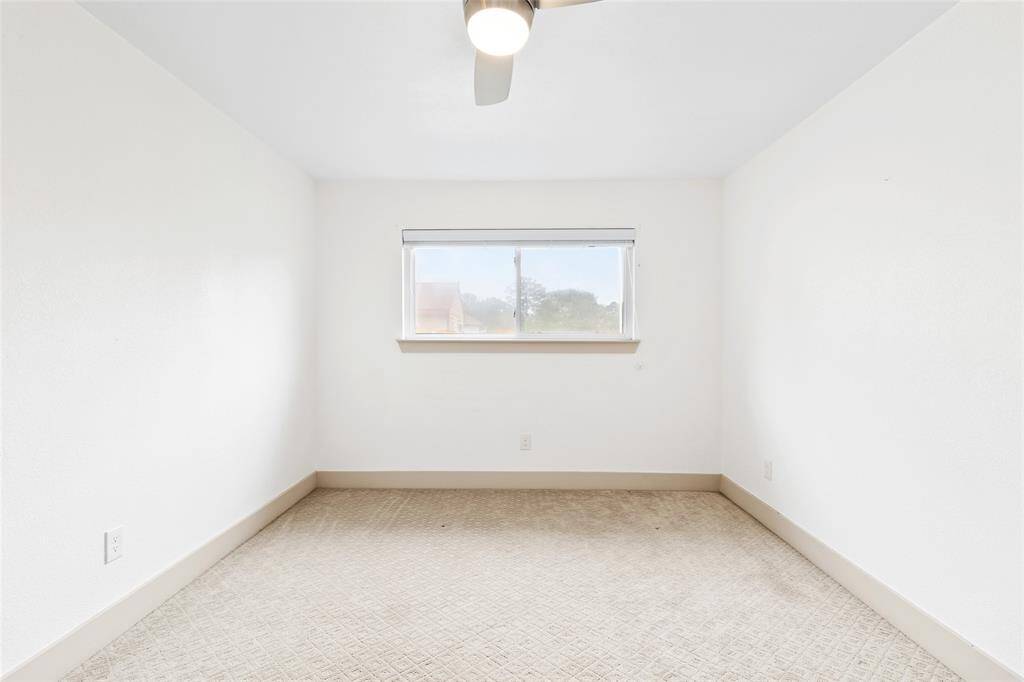 Your light-filled secondary bedroom offers a calm, neutral setting with plush carpeting and a wide window that lets in soft, natural light. A modern ceiling fan ensures comfort, while the simple layout invites personalization as a guest room, office, or creative space.