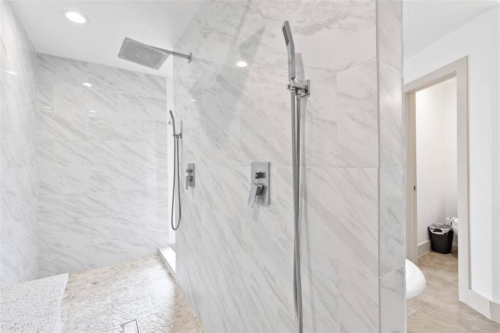 Your spacious walk-in shower is designed for both comfort and luxury, featuring elegant marble-look tile walls and a pebble stone floor. The built-in bench adds a relaxing touch, while dual showerheads—one rainfall and one handheld—offer a spa-like experience.