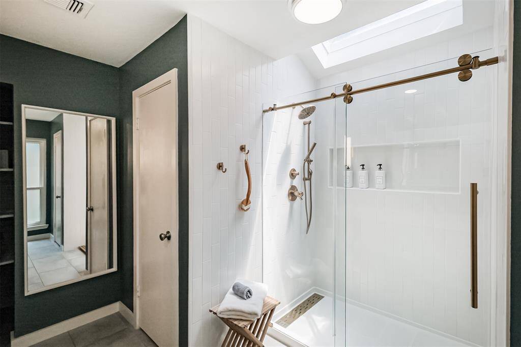 The standing shower in the primary bathroom has brushed gold fixtures, tile surround and a sliding glass door.