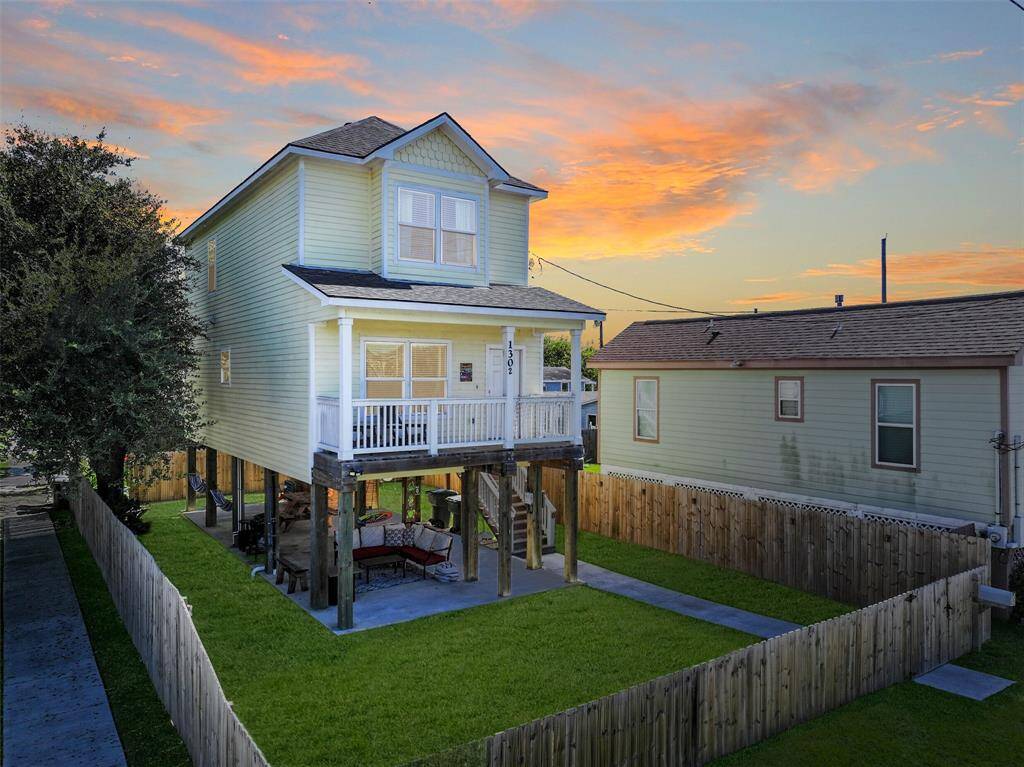 Elevated two-story home with a charming front porch, set on a fenced corner lot in the heart of Galveston features a covered outdoor area that's perfect for relaxation.