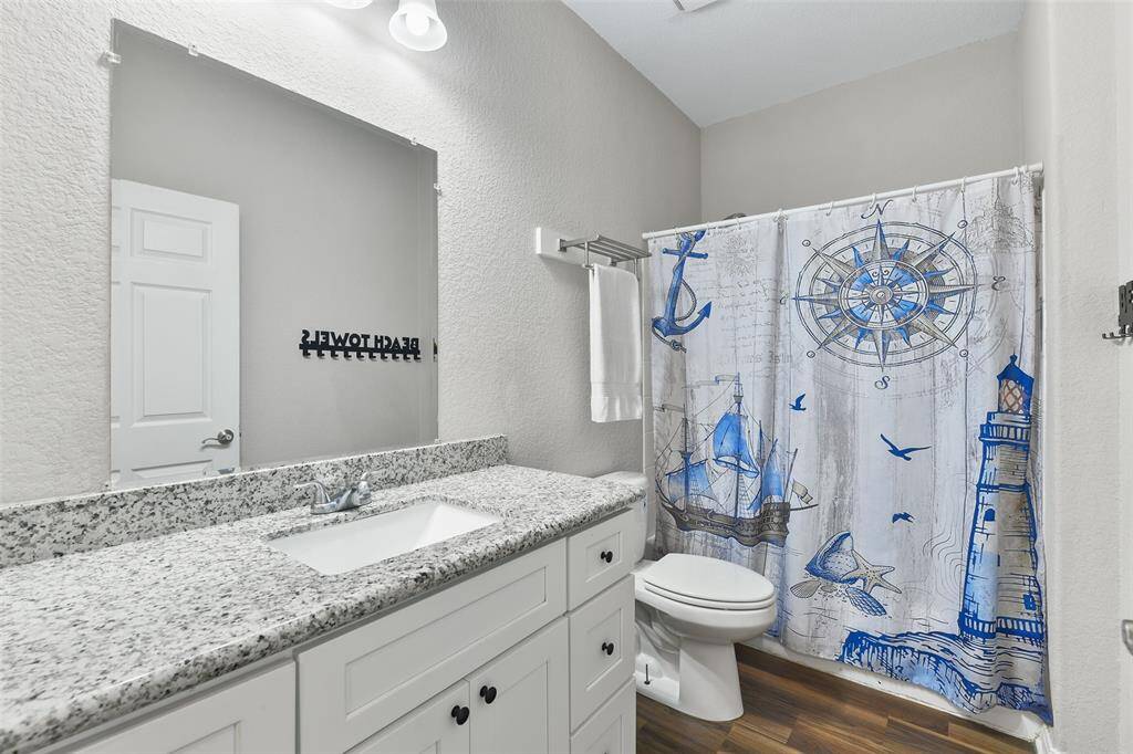This bathroom features a stylish nautical theme with a granite countertop, white cabinetry, and a combinaitob bathtub and shower with a blue and white shower curtain. The space is bright and modern, offering a clean and inviting atmosphere.