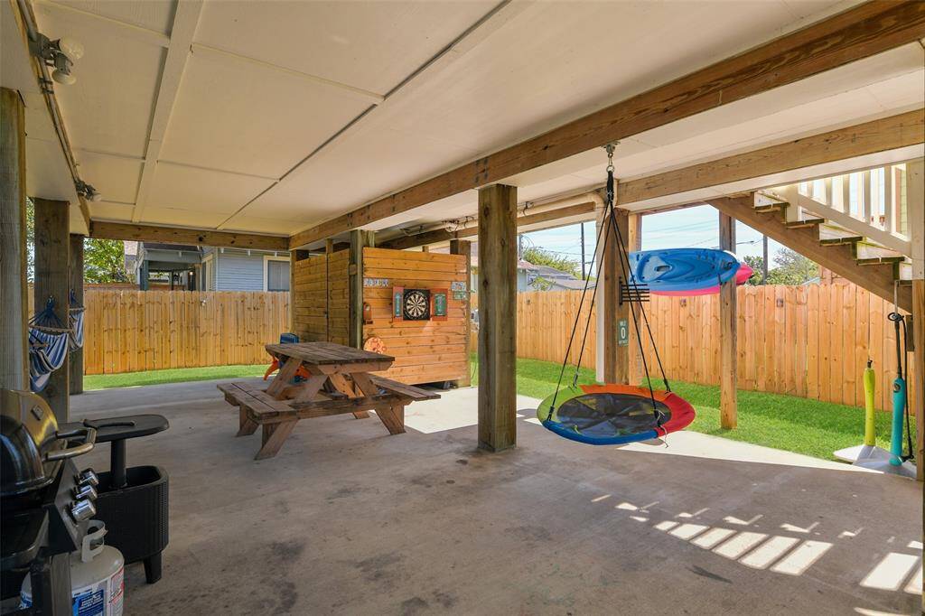 This photo highlights the covered outdoor entertaining space with a concrete floor, a picnic table, hanging swing, grill, dartboard, outdoor shower. Also note the included hammocks & kayak!